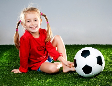 little girl with soccer ball in boots on a green lawnの写真素材
