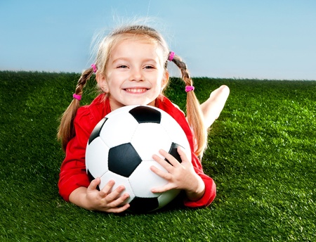 little girl with soccer ball in boots on a green lawnの写真素材