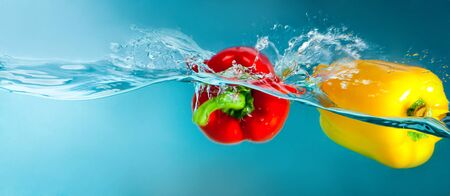 colorful peppers splashing into blue waterの写真素材
