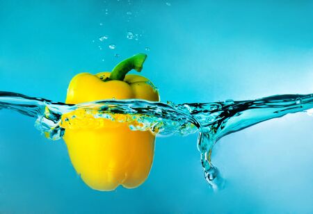 yellow pepper splashing into blue waterの写真素材