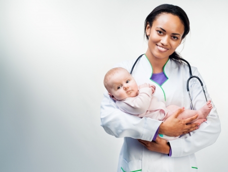 Smiling doctor with small baby isolated on a light backgroundの写真素材