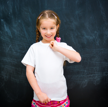 cute little girl standing in a white t shirt against the school board