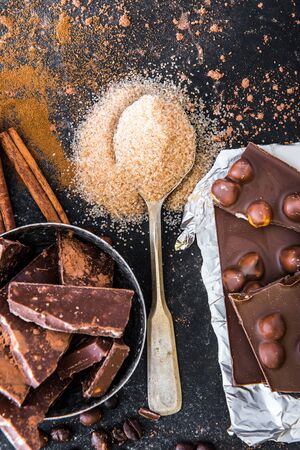 Nuts in chocolate and spices in the spoons on a dark table