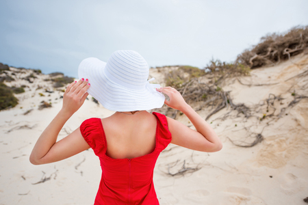 beautiful young woman in evening red dress and white hat on a background of a sand desertの写真素材