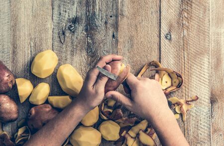 hands peeling potato on wooden boardの写真素材