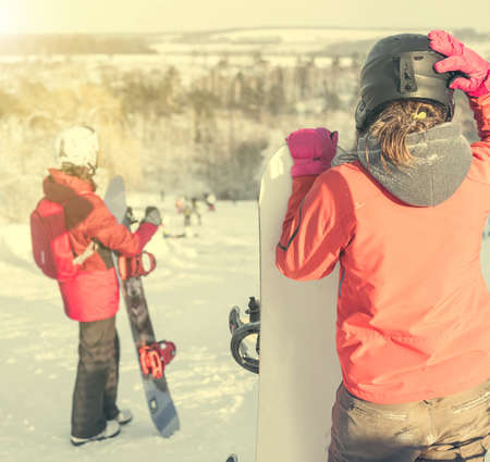 people in ski suit holding snowboards on a snowhill view from backの写真素材