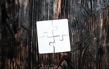 four connected pieces of white jigsaw on dark wooden tableの写真素材