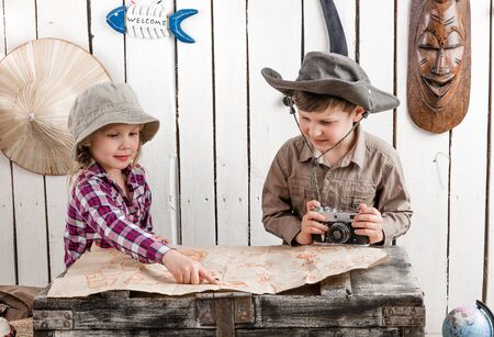 two little children in hats watching map on big old chestの写真素材