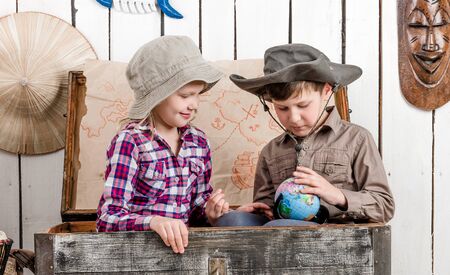 little boy and girl study globe sitting in big old chest