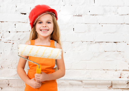 little girl-worker in orange uniform with paint roller in handsの写真素材