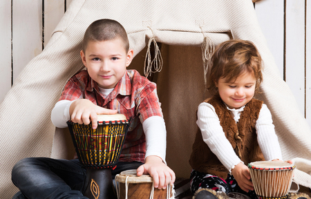 boy sitting on the floor and playing drum near wigwam in decorated wooden roomの写真素材