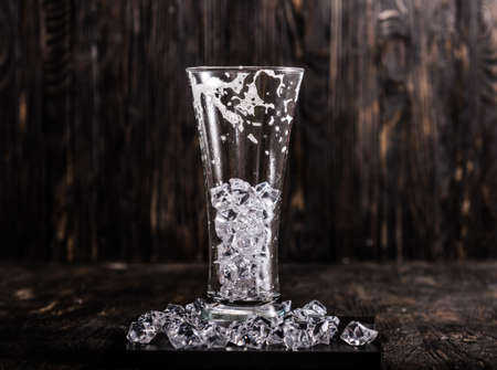 used empty glass with ice and beer foam on dark wooden backgroundの写真素材