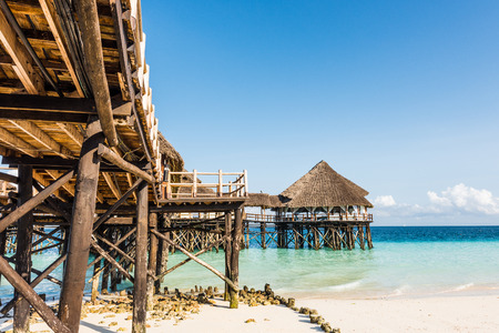 beautiful view of wooden pier with thatched roof in ocean and blue skyの写真素材