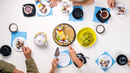 people eating dessert and drinking tea together at white table, top viewの写真素材