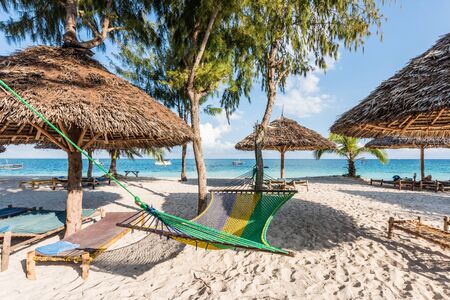 handmade wooden chaise longues, straw umbrellas and hammock on a beach near oceanの写真素材
