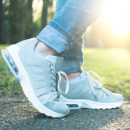 Person walking in nice gray comfortable running shoes in the green park in sunlight, closeup