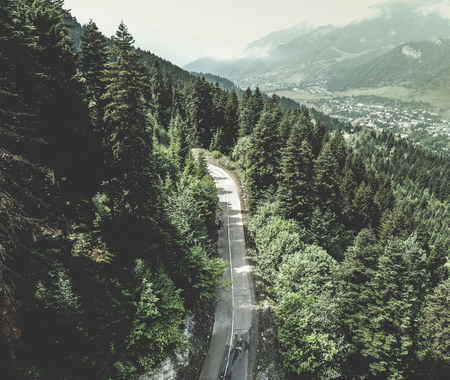 Aerial view over mountain road going through spruce forest landscape. Top view. Village on the...
