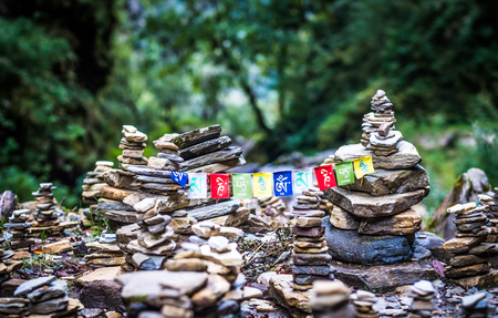 Sanskrit calligraphy of Buddhist Mantra Om Mani Padme Hum on multicolored flags hanging between two meditation stone pile on Annapurna track.の写真素材