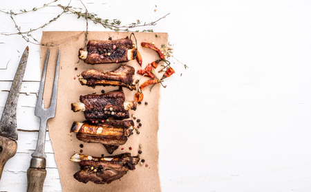 Top view of grilled pork ribs with herbs on the piece of brown crafted paper on white wooden background with cracked paint. Place for text and design.の写真素材