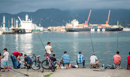 Batumi, Georgia - August 28, 2017: Company of local men fishing from the seaside promenade in Batumi, Georgia. View on the industrial port.のeditorial素材