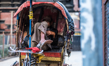 Kathmandu, Nepal - 06 October 2017: Middle-aged rickshaw driver sits with crossed legs in the cabin...