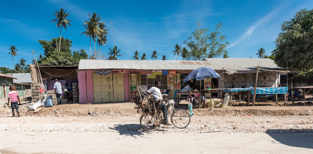 Zanzibar, Tanzania - July 14, 2016: Man carrying wood and trash on his bicycle, old half-ruined shack on background, Zanzibar, Tanzaniaのeditorial素材
