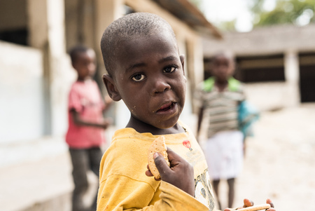 Zanzibar, Tanzania - July 14, 2016: Local kid in a yellow shirt, eating cookie in Zanzibar, Tanzaniaのeditorial素材