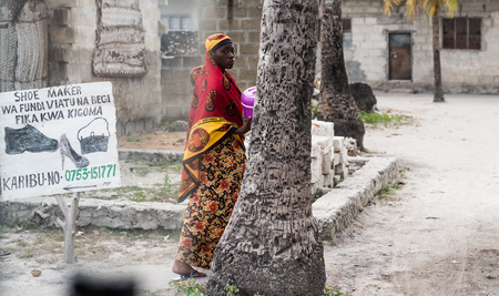 Zanzibar, Tanzania - July 14, 2016: Muslim woman walking near a showmaker banner in Zanzibar, Tanzaniaのeditorial素材