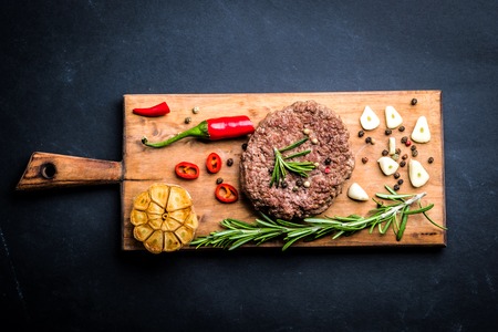 Delicious beef burger steak with spices and herbs on cutting board and slate background, top viewの写真素材