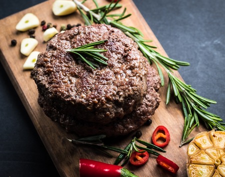 Delicious beef burger steak with spices and herbs on cutting board and slate backgroundの写真素材