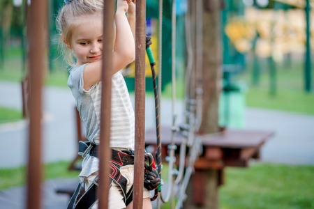 Cute girl enjoying activity in a climbing adventure park. Girl goes on hinged trail.の写真素材