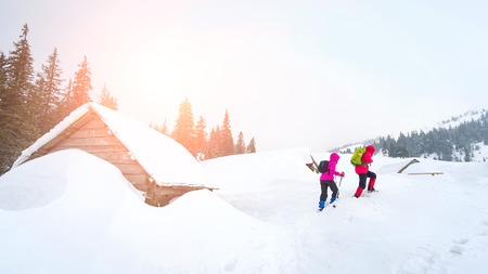 Hikers going by old wooden mountain hut covered with snow in Carpathian mountainsの写真素材