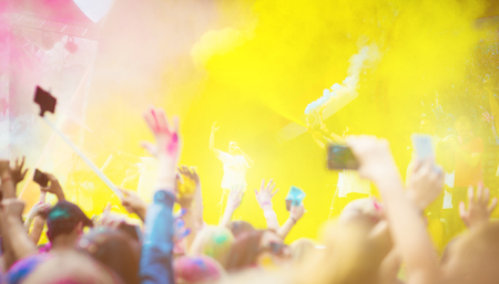 Crowd of people dancing and celebrating Holi festival of colors. People taking photos with mobile...
