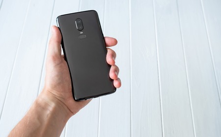 Black modern smartphone holing in a hand on white wooden table background