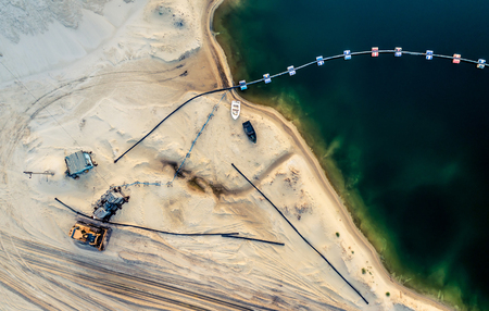 Aerial view of machinery and mine equipment near deep blue lake on sandy surfaceの写真素材