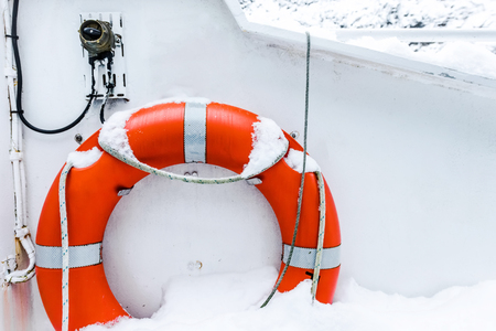 Lifebuoy ring on white boat in winter covered with snow. Safety equipment on the boat. Orange life buoy on a sailing boatの写真素材