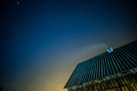 Smoke from the chimney at moon night. Old rural roof under starry sky in mountainsの写真素材