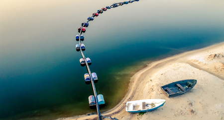 Aerial view of blue tube with barrels on the lake and two boates on sandy beachの写真素材