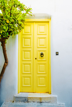 Front view of the white building with yellow door and green tree on greek streetの写真素材
