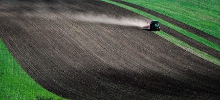 Sunshine view of big tractor plowing the ground of green field on the slopeの写真素材