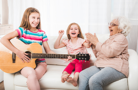Joyful granddaughters with grandmother listening the guitar playの写真素材