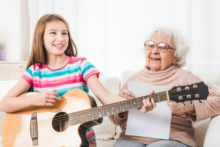 Smiling granddaughter playing on guitar for grandmotherの写真素材