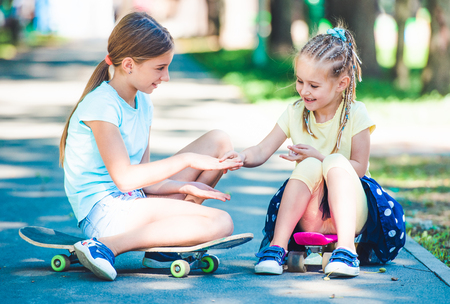 Smiling little kids sitting on skateboards and playing in the parkの写真素材