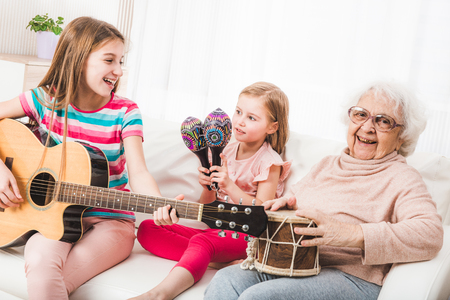 Smiling grandmother with granddaughters singing and playing on music instruments togetherの写真素材