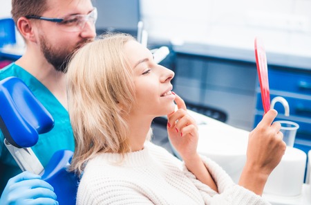 Satisfied blond girl looking in red mirror after dentists workの写真素材