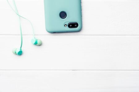 Azure digital telephone with body protection and blue headphones at the white table, close-up with space for patternの写真素材