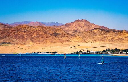 Windsurfers with a sails moves on the sea against rocky seashore