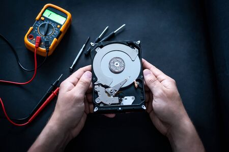 Man hands and digital mutimeter fixing hard drive