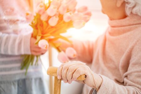 Bouquet in girls hands behind cane in old womans hand