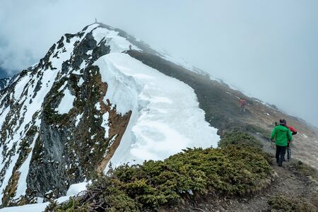Group of tourists reaching top of majestic greened snowy mountain